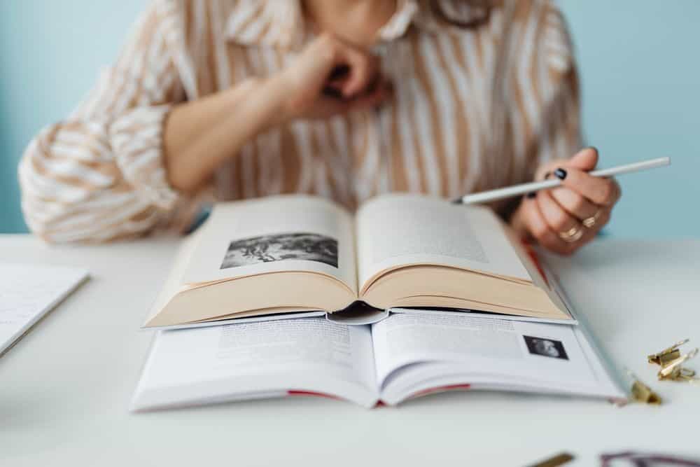 A person engaged in studying with books and a pen, focused and learning.